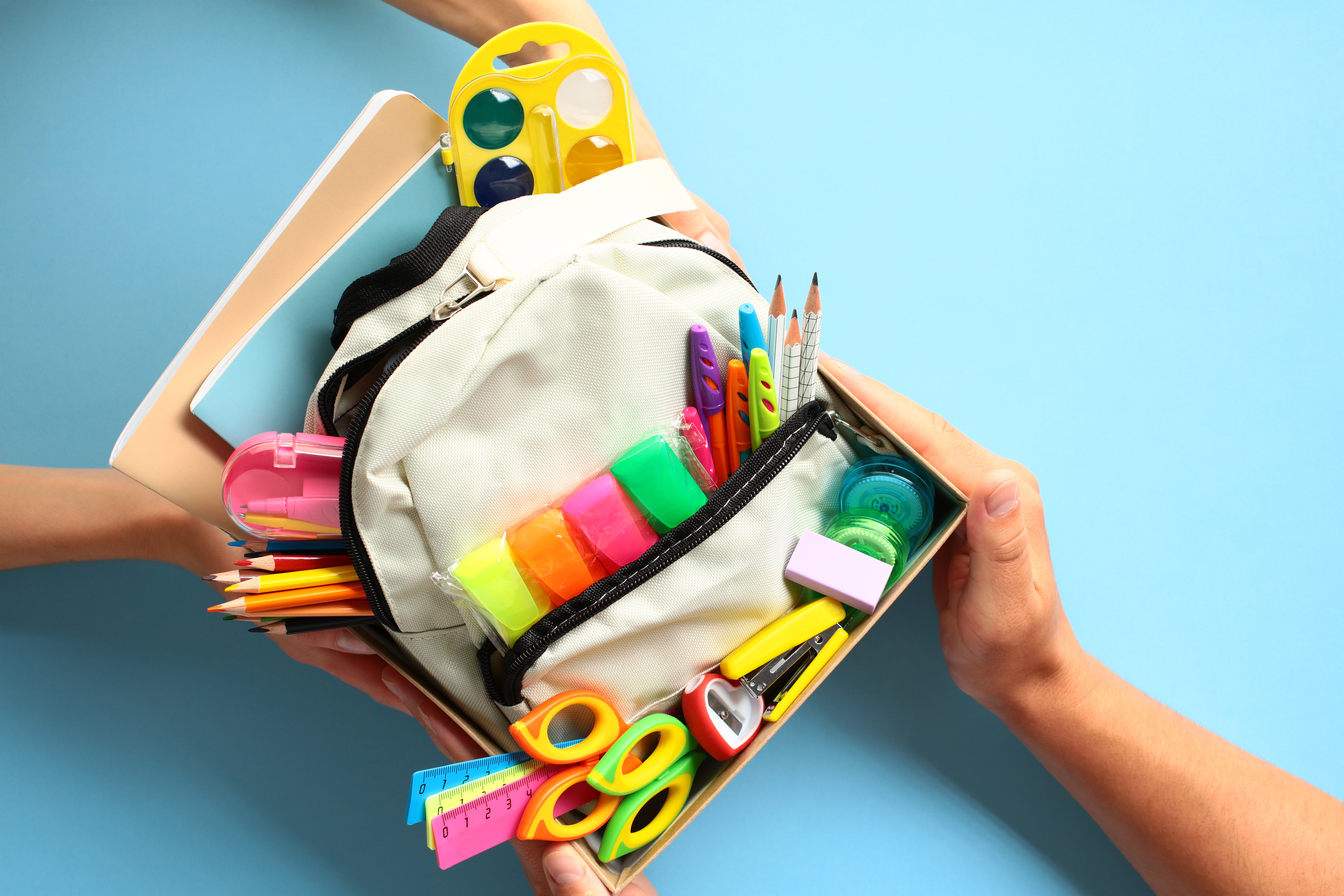 Back to school donation drive concept. Top view cardboard box with backpack full of colorful school supplies.